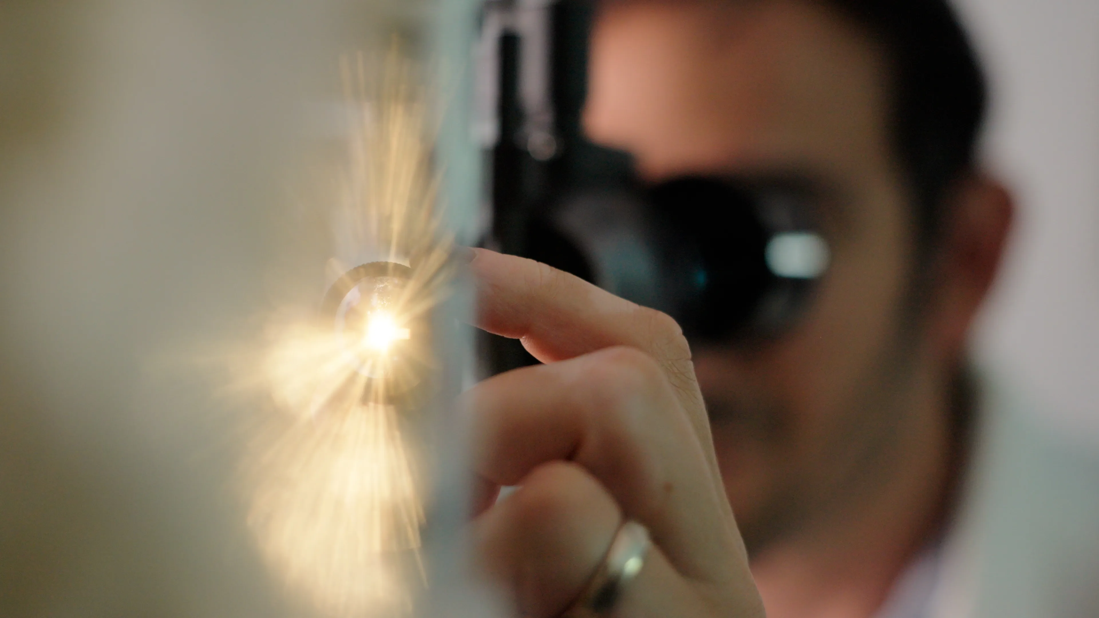 Ein Augenarzt untersucht einen Patienten mit einer Spaltlampe, während ein intensiver warmer Lichtstrahl aus seiner Lampe auf der linken Seite des Bildes scheint.